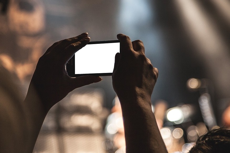 Hände, die ein Smartphone halten und eine Bühne filmen