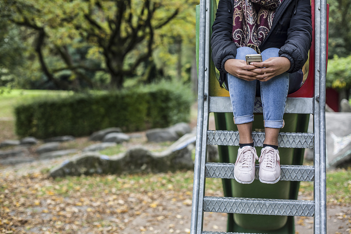 Ein Mädchen sitzt auf den Stufen einer Rutschbahn und umklammert ihr Handy.